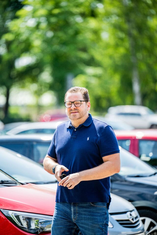 Mann mit Smartphone steht auf Parkplatz.